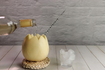 Melon with wine, melvin, cocktail, placing white wine, bottella, whole melon, ice. On round wicker on white wooden board Originating from Chile in summer. typical chilean food and drink