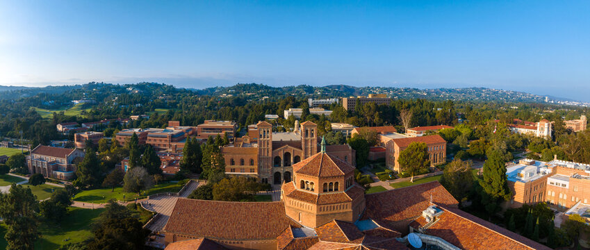 Aerial view of UCLA campus in Westwood, Los Angeles, featuring red-brick, Gothic, and modern buildings amidst green lawns and trees on a sunny day.