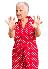 Senior beautiful woman with blue eyes and grey hair wearing a red summer dress afraid and terrified with fear expression stop gesture with hands, shouting in shock. panic concept.