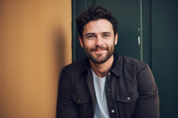 Fototapeta premium Relaxed man with a beard sitting by a colorful wall in casual fashion