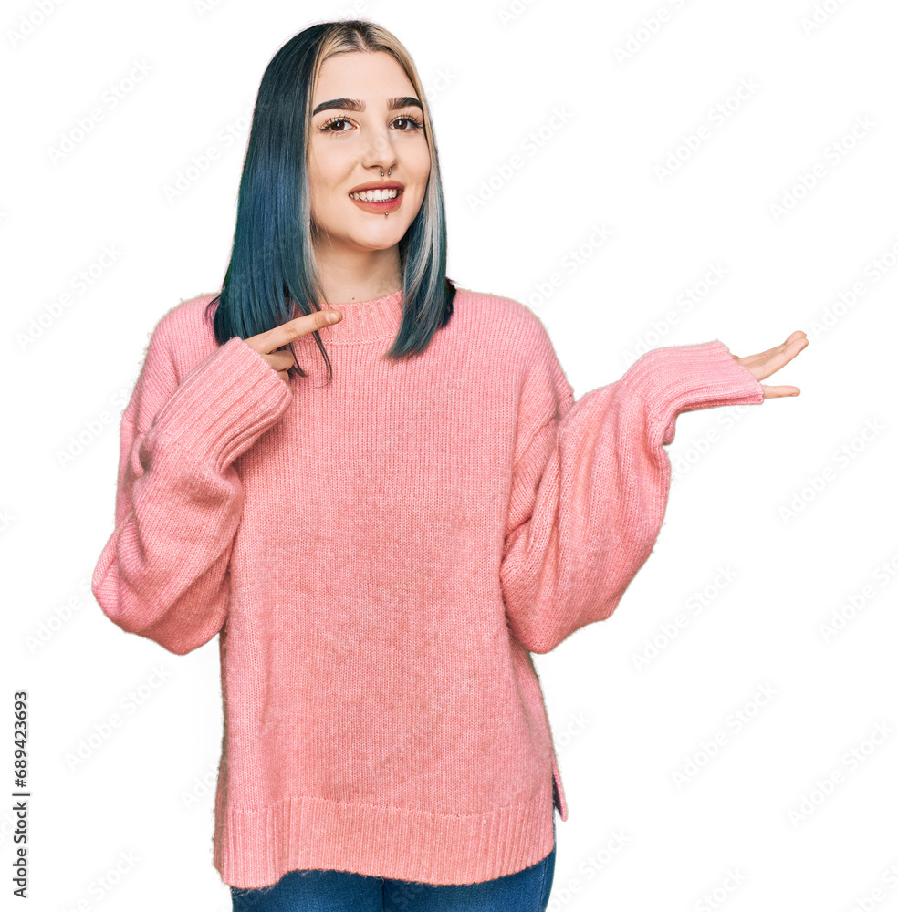 Wall mural Young modern girl wearing pink wool winter sweater amazed and smiling to the camera while presenting with hand and pointing with finger.