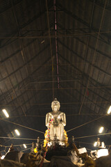 A large silver seated Buddha statue in the Pa Lelai pose. Inside the sermon hall At the bottom,...