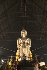 A large silver seated Buddha statue in the Pa Lelai pose. Inside the sermon hall At the bottom,...