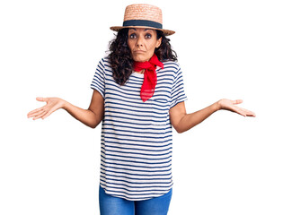 Middle age beautiful woman wearing casual striped t shirt and summer hat clueless and confused...