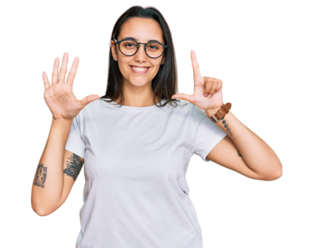 Young hispanic woman wearing casual white t shirt showing and pointing up with fingers number seven while smiling confident and happy.