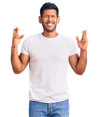 Young latin man wearing casual clothes gesturing finger crossed smiling with hope and eyes closed....