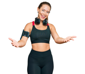 Beautiful blonde woman wearing gym clothes and using headphones smiling cheerful offering hands giving assistance and acceptance.