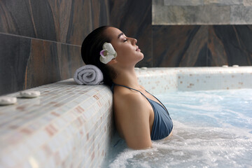 Beautiful woman with orchid flower relaxing in spa swimming pool