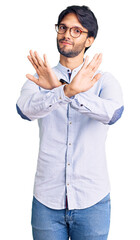 Handsome hispanic man wearing business shirt and glasses rejection expression crossing arms and palms doing negative sign, angry face