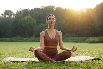 Beautiful young woman practicing Padmasana on yoga mat outdoors. Lotus pose