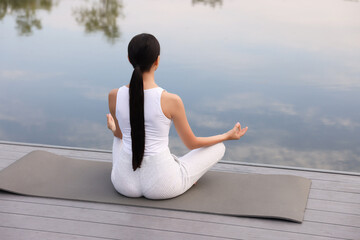 Fototapeta na wymiar Woman practicing Padmasana on yoga mat outdoors, back view. Lotus pose