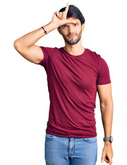 Fototapeta premium Handsome hispanic man wearing casual clothes making fun of people with fingers on forehead doing loser gesture mocking and insulting.