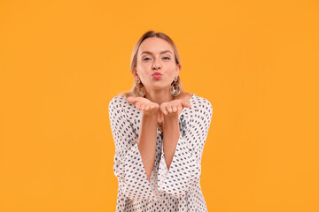Portrait of beautiful hippie woman blowing kiss on yellow background
