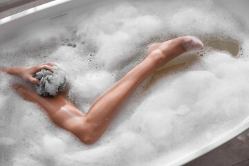Woman taking bath with mesh pouf in tub, top view