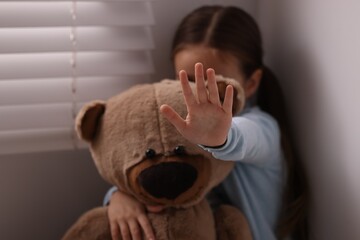 Child abuse. Little girl with teddy bear doing stop gesture indoors, selective focus - obrazy, fototapety, plakaty