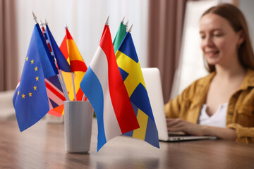 Woman working with laptop at table indoors, focus on different flags - obrazy, fototapety, plakaty