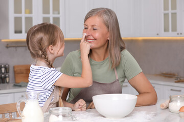 Happy grandmother with her granddaughter having fun while cooking together in kitchen