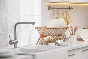 Sink and drying rack with clean dishes and cutlery on countertop in kitchen