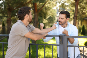 Angry neighbours having argument near fence outdoors