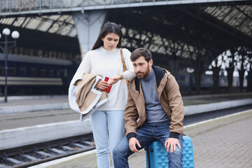 Being late. Worried couple with suitcase waiting at train station
