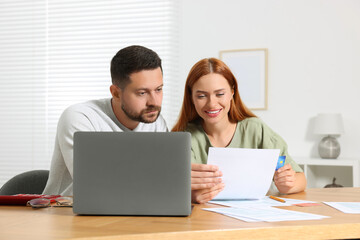 Couple with credit card using laptop for paying taxes online at home