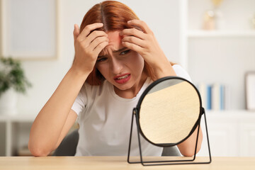 Suffering from allergy. Young woman with mirror checking her face at home