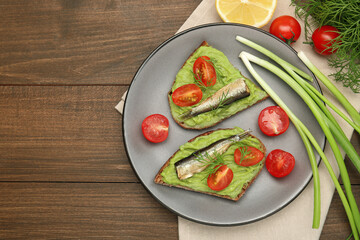 Delicious sandwiches with sprats, tomatoes, avocado puree and dill on wooden table, flat lay. Space for text