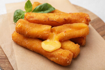 Tasty fried mozzarella sticks and basil on light table, closeup