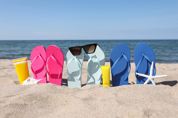 Stylish colorful flip flops with sunglasses and sunscreens on beach sand