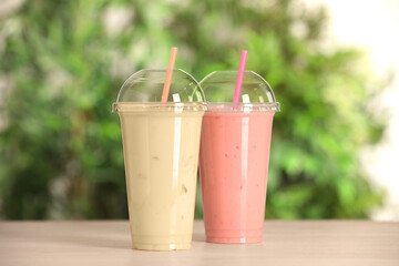 Plastic cups with different tasty smoothies on wooden table outdoors