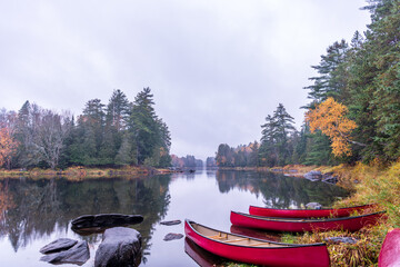 canoes on the shore of a calm reflective part of the lower madawaska river ontario in fall with...