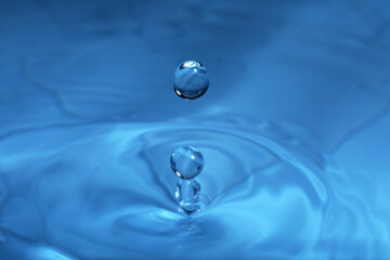 Drop falling into water on blue background, macro view