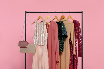 Rack with stylish women's clothes on wooden hangers and accessories against pink background