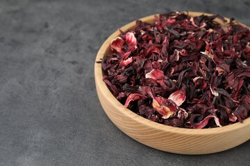 Hibiscus tea. Wooden bowl with dried roselle calyces on grey table, closeup. Space for text