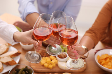 People clinking glasses with rose wine above wooden table indoors, closeup