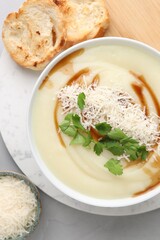 Delicious cream soup with parmesan cheese, soy sauce in bowl and croutons on light grey table, flat...
