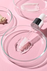 Pipette, cosmetic serum and petri dishes with samples on pink background, closeup