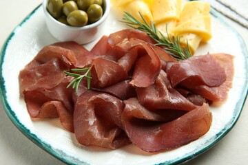Delicious bresaola, cheese, olives and rosemary on light table, closeup