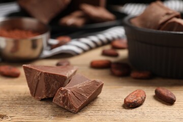 Pieces of tasty milk chocolate and cocoa beans on wooden table, closeup
