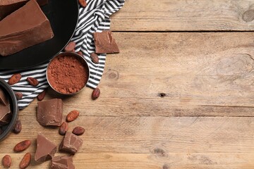 Pieces of tasty milk chocolate, cocoa beans and powder on wooden table, flat lay. Space for text