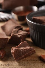Pieces of tasty milk chocolate and cocoa beans on wooden table, closeup