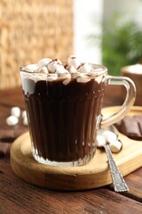 Cup of aromatic hot chocolate with marshmallows and cocoa powder served on wooden table, closeup