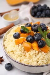 Bowl of tasty couscous with blueberries, pumpkin and mint on table, closeup