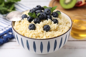 Bowl of tasty couscous with blueberries and mint on white table, closeup
