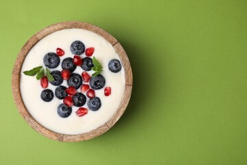 Bowl of delicious semolina pudding with blueberries, pomegranate and mint on green background, top view. Space for text