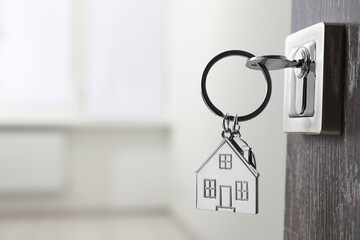 Mortgage and real estate. Open door with key and house shaped keychain against blurred background,...