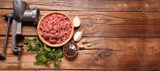 Manual meat grinder, beef mince, peppercorns, onion and parsley on wooden table, flat lay. Banner...