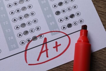 School grade. Answer sheet with red letter A, plus symbol and marker on wooden table, closeup