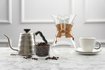 Glass chemex coffeemaker, kettle, beans in bowl and cup on white marble table