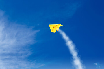 Yellow paper plane flying in blue sky with clouds